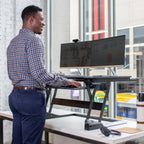 Man using a standing desk with dual monitors in an office setting
