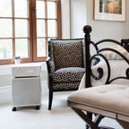 Room interior with a leopard print chair, white ottoman, and a small appliance on a white floor.