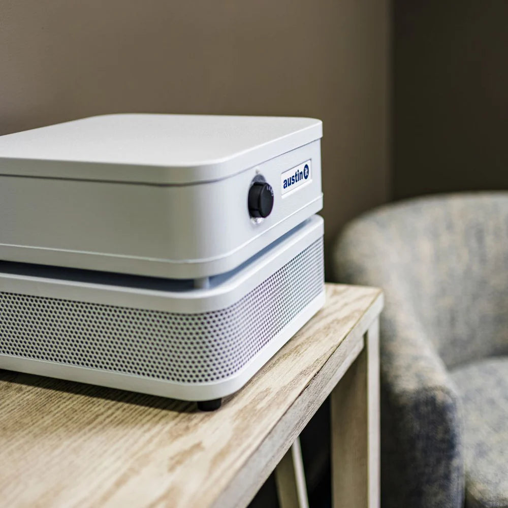White air purifier on a wooden table with a blurred chair in the background