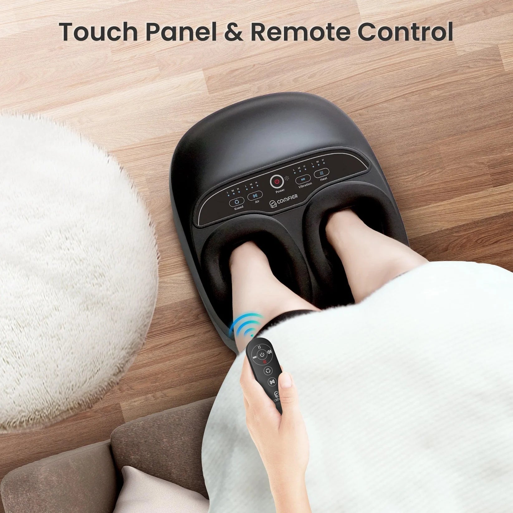Person using a foot massager with remote control on a wooden floor.