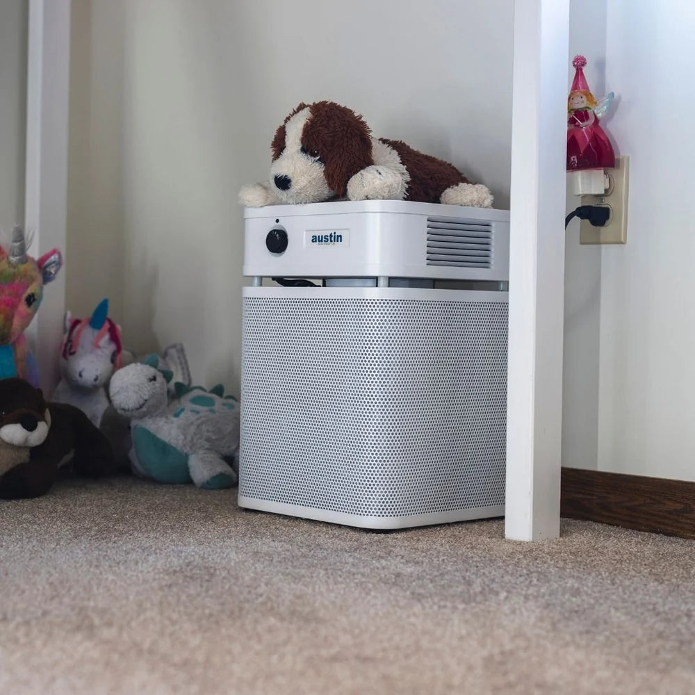 Air purifier with a plush dog toy on top in a room with stuffed animals.